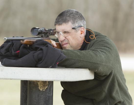 A man looks through a sight on his rifle at a shooting range.