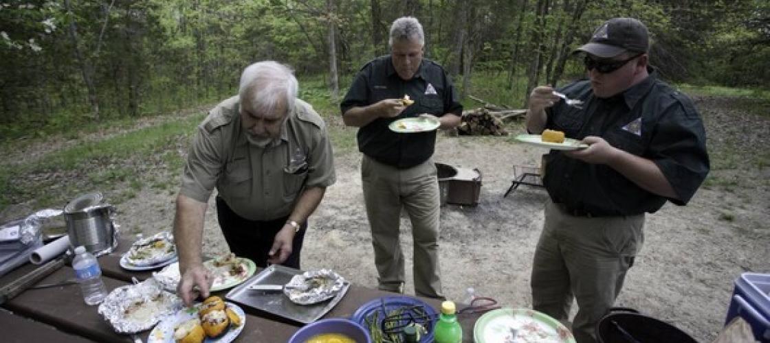 Three MDC staff members eat food after campfire cooking